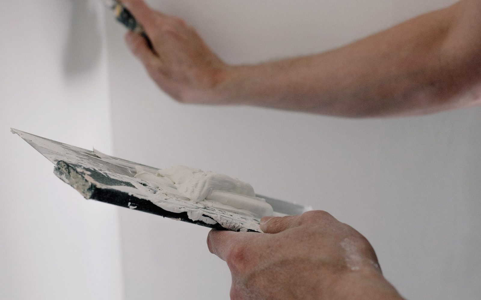 Plasterer's hands holding trowels loaded with finish plaster at a wall
